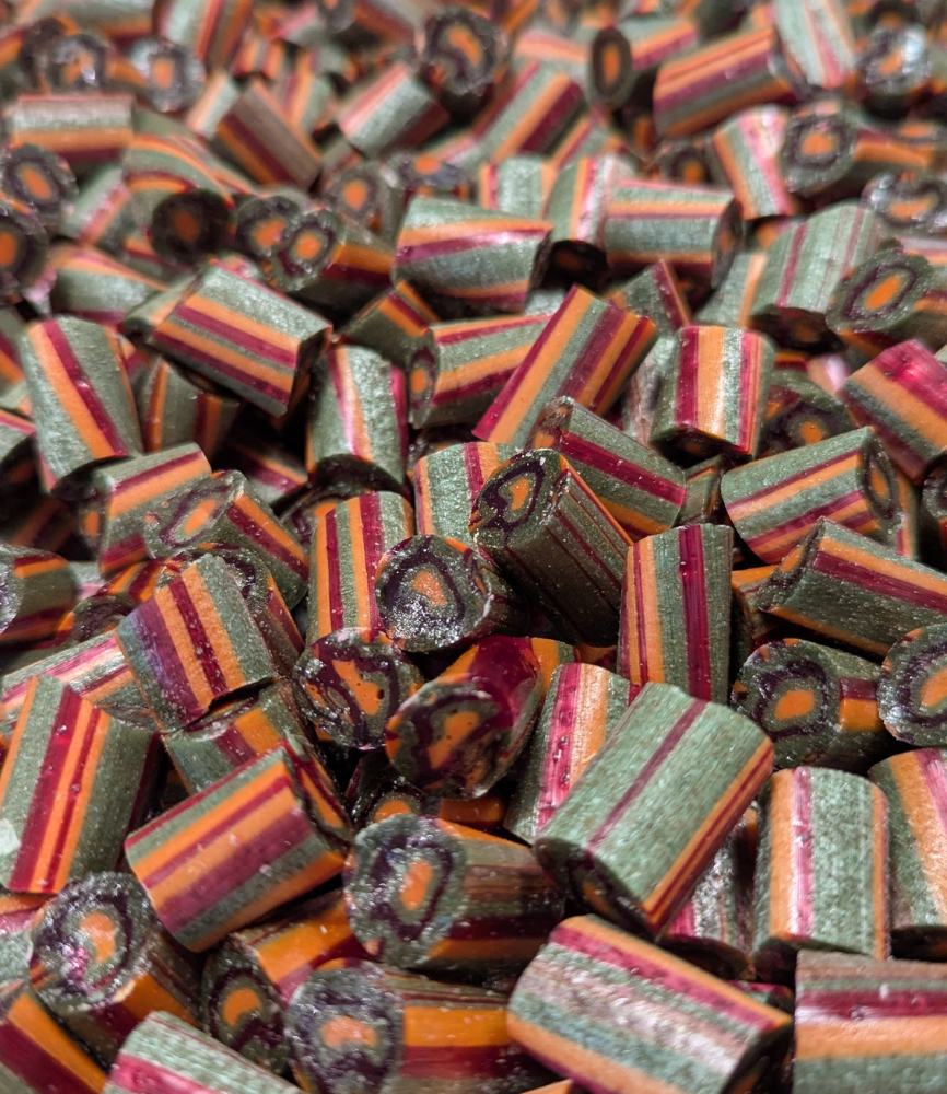 Håndlavede Lakrids og Mango bolcher fra Sømods Bolcher. Grønne lakrids bolcher med røde og orange striber, lavet af rent perlesukker og naturlige ingredienser. Sommernyhed med sød mango og lakrids – dansk gourmet slik.